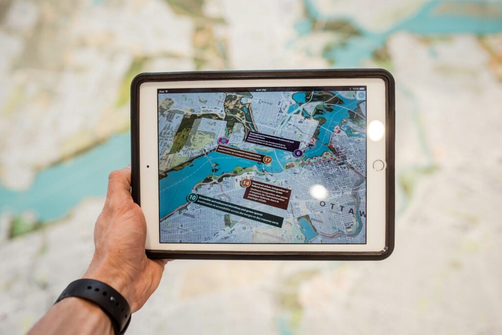 A hand holding a tablet displaying a city map of Ottawa, with various highlighted points on a blurred background map.