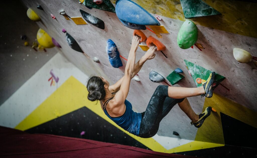 A climber hangs from a colorful indoor bouldering wall, focused as she reaches for the next handhold.
