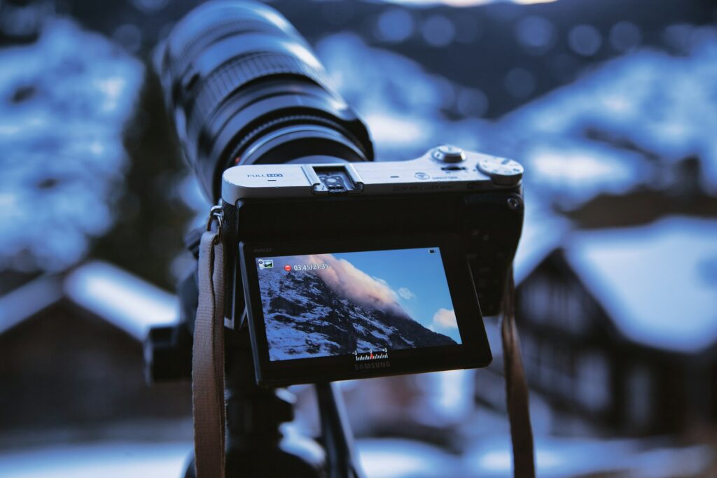 A camera holds a photograph of a majestic mountain landscape, showcasing its peaks and natural beauty.