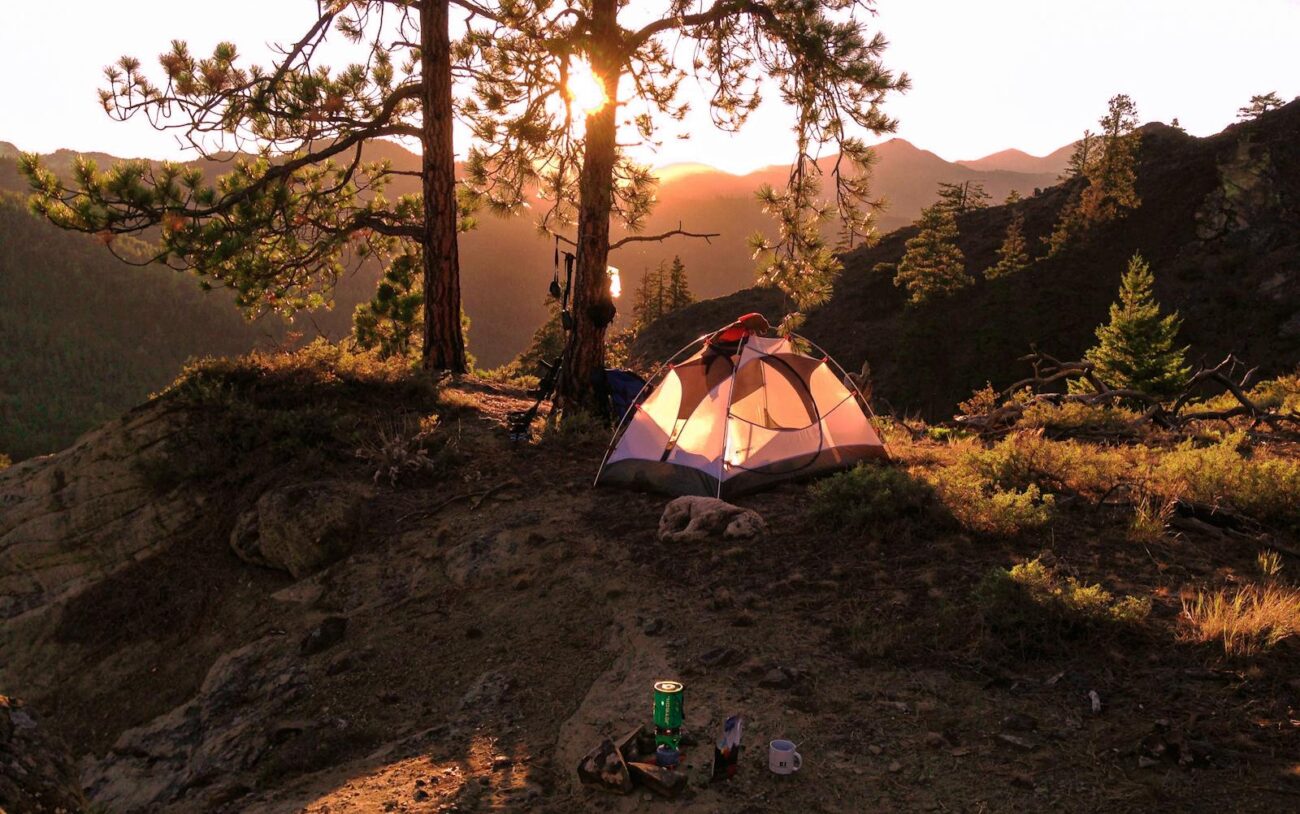 Tent nestled in forested mountains at sunrise, capturing the serene beauty of camping outdoors.