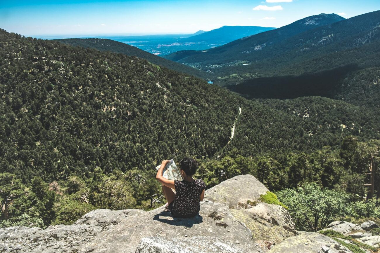 A woman sits on a rock with a map, enjoying a breathtaking mountain view.