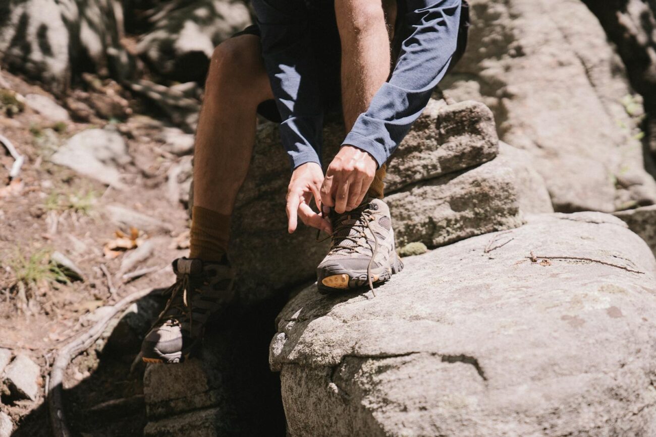 Close-up of a hiker tying boots on a rocky trail, emphasizing outdoor adventure.