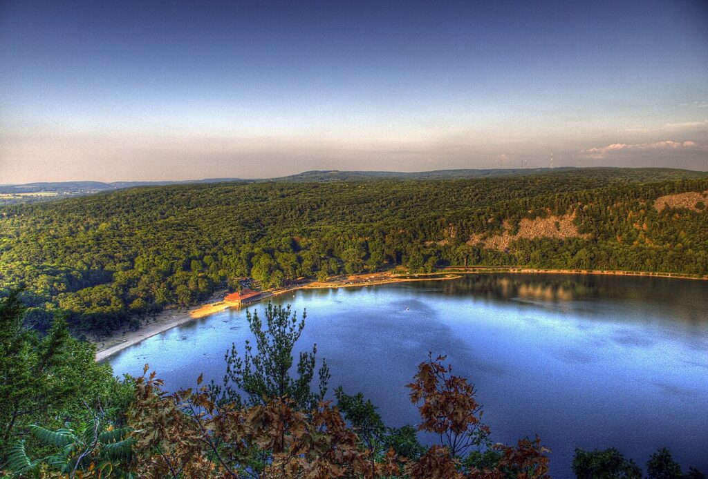 A serene landscape showing a calm lake surrounded by lush greenery and distant hills under a clear sky during sunset.
