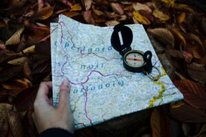 A compass and a map resting on a bed of green leaves, suggesting exploration and adventure in nature.
