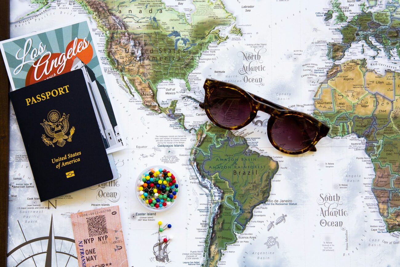 A travel-themed layout featuring a U.S. passport, sunglasses, a Los Angeles postcard, and a world map with colorful pushpins.