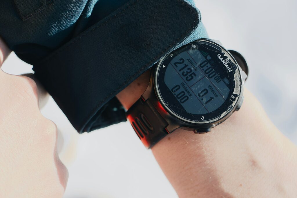 A close-up of a Garmin smartwatch on a wrist, displaying altimeter, distance, and speed metrics in a rugged outdoor setting.