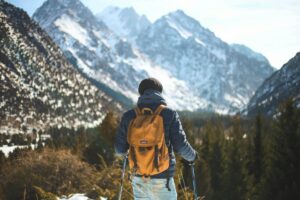 A man stands in the snow, equipped with a backpack and ski poles, ready for an outdoor adventure.